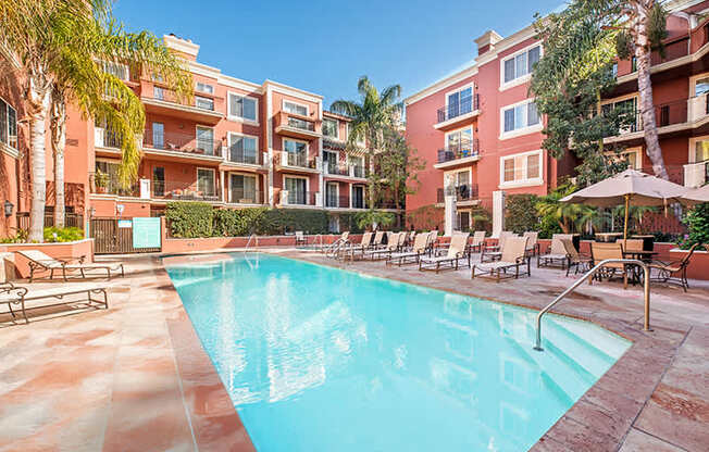 A swimming pool surrounded by lounge chairs and umbrellas in front of a red building.