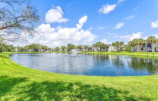 a lake with a fountain in the middle of a grassy field at Waterford Park Apartment Homes, LLC, Lauderhill Florida