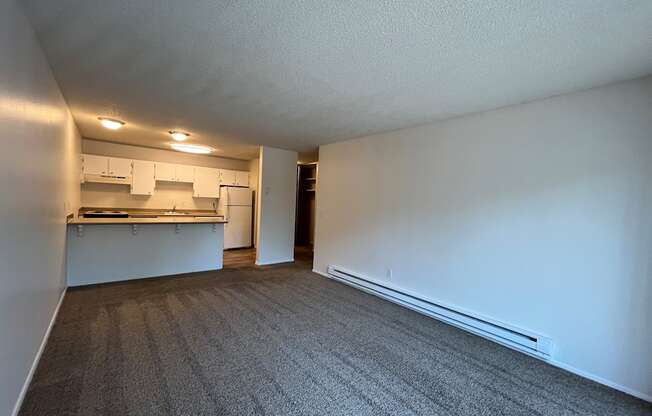 an empty living room with a kitchen in the background