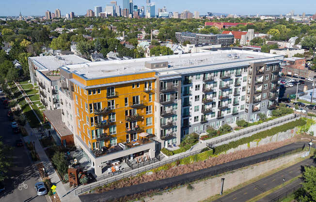 A modern apartment building with a mix of orange and white balconies is surrounded by a concrete wall and a grassy area.
