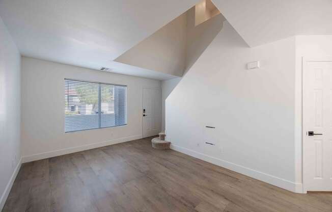 a living room with white walls and a window and wood floors