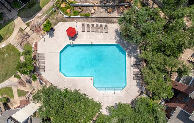 A red umbrella sits on the edge of a blue swimming pool.