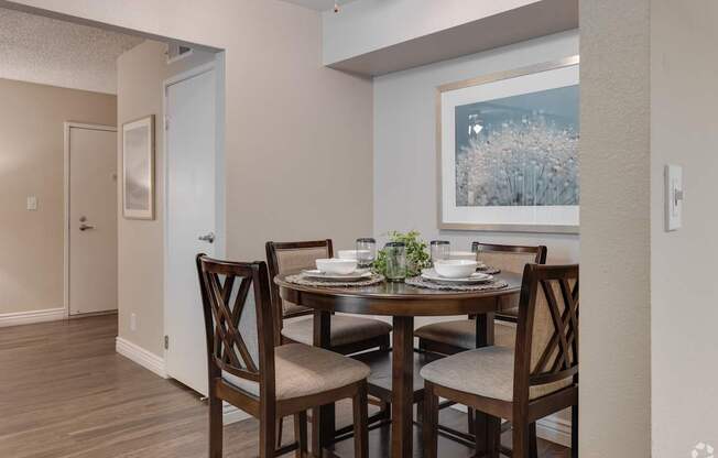 A dining room with a table set for two and a painting on the wall.