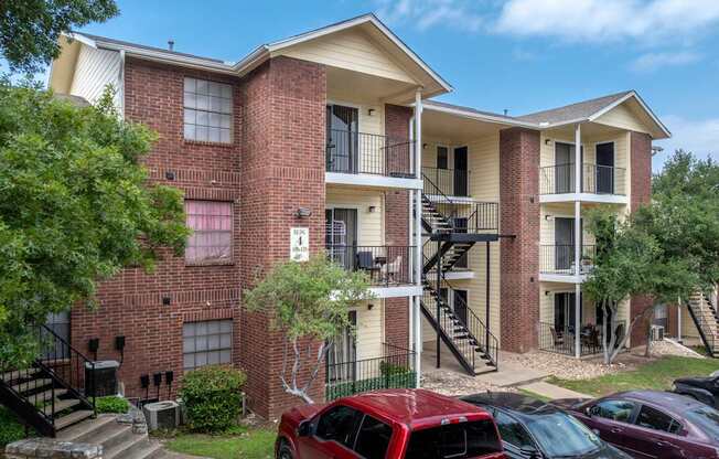 A red car is parked in front of a brick apartment building.