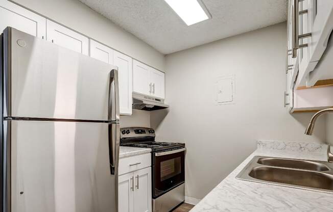 Aurora, CO Apartments – Ivy Crossing – A kitchen with a fridge, white cabinets, and a stove top oven.