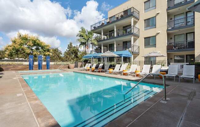 A large swimming pool in front of a building with sun loungers.