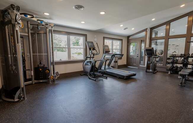 a gym with treadmills and other fitness equipment in a home with windows
