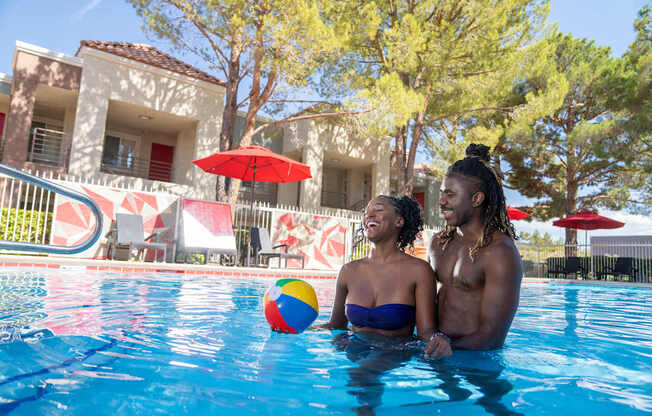 A couple is sitting in a pool with a ball in the foreground.