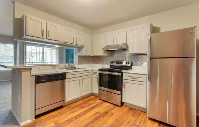 Premium Upgrade Kitchen with white countertops, white cabinets, stainless appliances, wood-style flooring, and pass-through bar to the living room