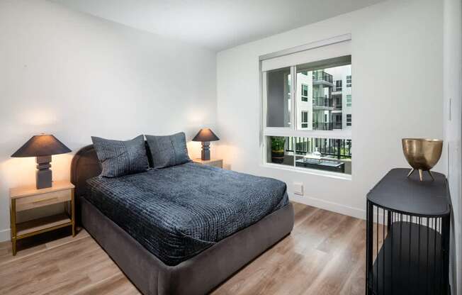 A bedroom with a large bed and a view of a building outside the window.