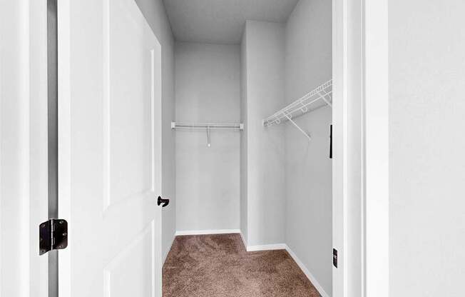 A white door with a black handle is open to a hallway with a carpeted floor.