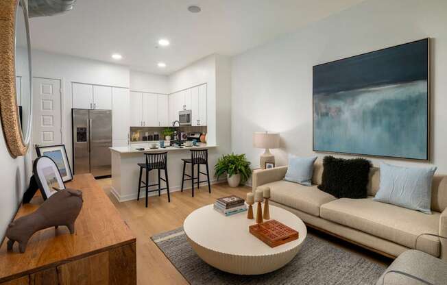 A modern living room with a large painting on the wall and a kitchen area in the background.