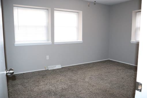 an empty room with a carpeted floor and two windows