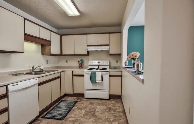 Grand Forks Primrose Apartments. A kitchen with a white stove top oven next to a sink and a dishwasher