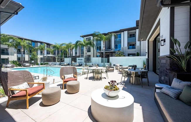 A poolside area with chairs and a table with a bowl of fruit on it.