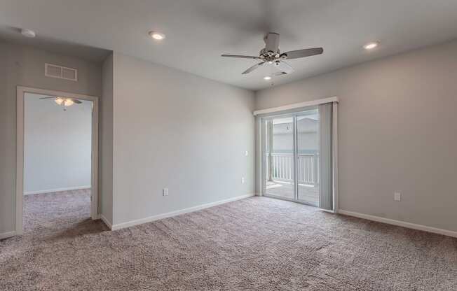 an empty room with a ceiling fan and a door to a balcony