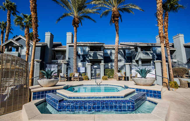A pool surrounded by palm trees and a building in the background.