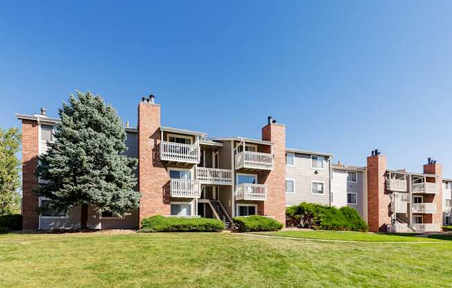 an exterior view of an apartment building with green grass and a tree