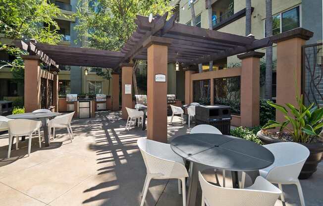 A patio with tables and chairs under a pergola. at The Kitt at Warner Center Apartments, Woodland Hills, CA, 91303
