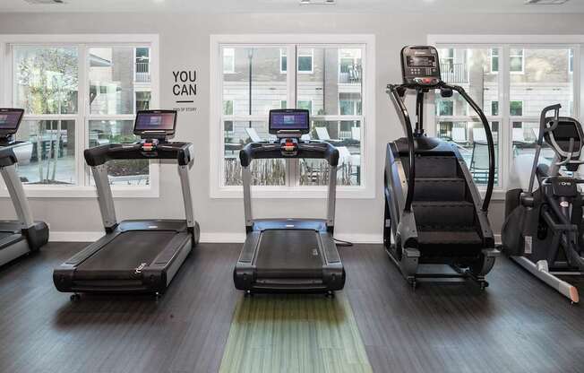 a gym with cardio equipment and large windows