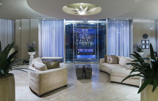 A wide lobby space with two curved, upholstered couches, a star-shaped light fixture, and floor-to-ceiling windows with drawn curtains.