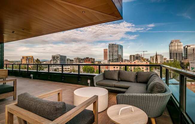 A balcony with a couch, chair, and table with a city view in the background.