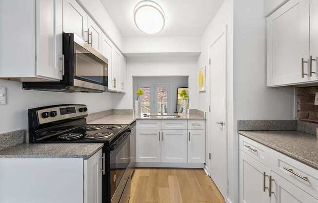 Modern galley kitchen at Monon Living in Broad Ripple featuring white shaker cabinets, granite countertops, and pass-through window with Monon Trail access nearby.