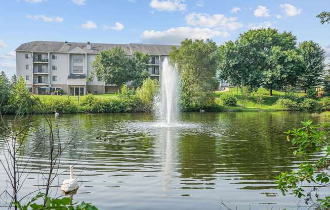 A fountain in the middle of a pond with a building in the background.