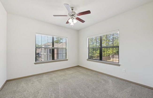 A room with a ceiling fan and two windows.