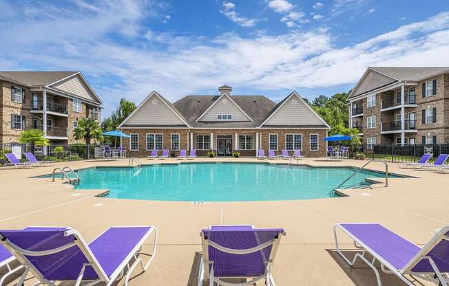 A large swimming pool surrounded by purple lounge chairs in front of apartment buildings.