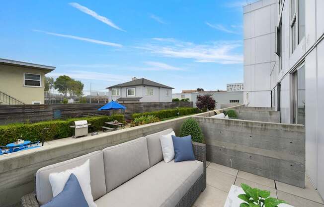 A modern outdoor seating area with a concrete wall and a grey couch.