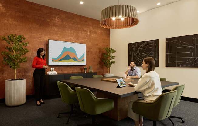 A woman in a red top stands in front of a whiteboard with a graph on it, while two other people sit at a table with laptops.