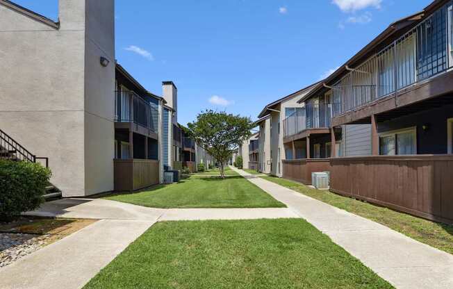 An area of grass and sidewalks between apartment buildings at Windridge on the Parkway in Dallas, TX
