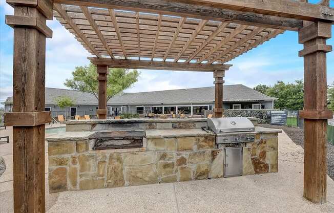 an outdoor kitchen with a stone wall and a pergola