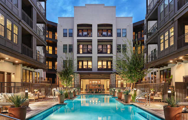 A large swimming pool is surrounded by potted plants and lounge chairs in the middle of a courtyard.