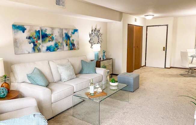 A living room with a white couch, a glass coffee table, and a painting on the wall.