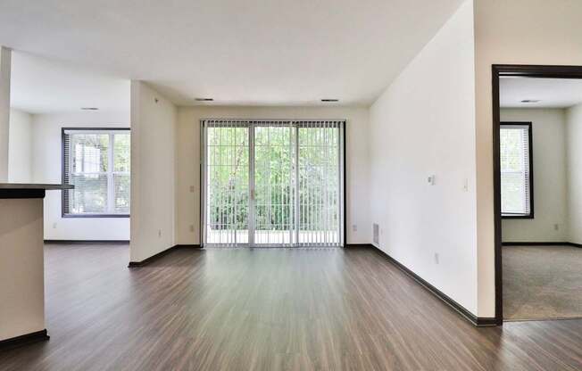 A spacious room with wooden floors and a large window with blinds.