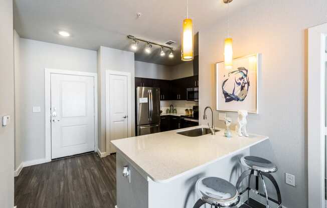 Kitchen island with white quartz countertops, modern lighting fixtures looking into kitchen