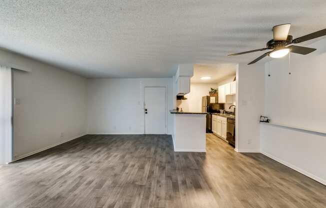 an empty living room with a ceiling fan and a kitchen