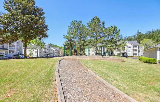 A gravel path leads through a grassy area with trees and houses in the background.