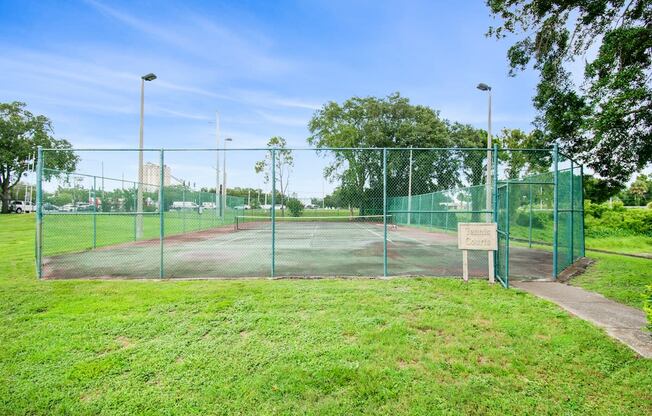 a tennis court on a grass field next to a fence