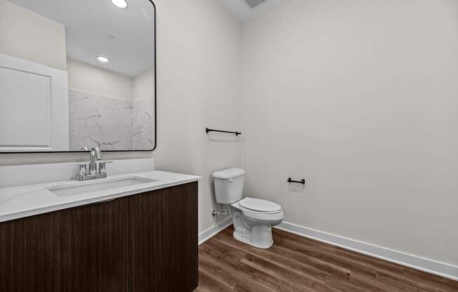 A white toilet sits in a bathroom with a wooden vanity and marble counter.
