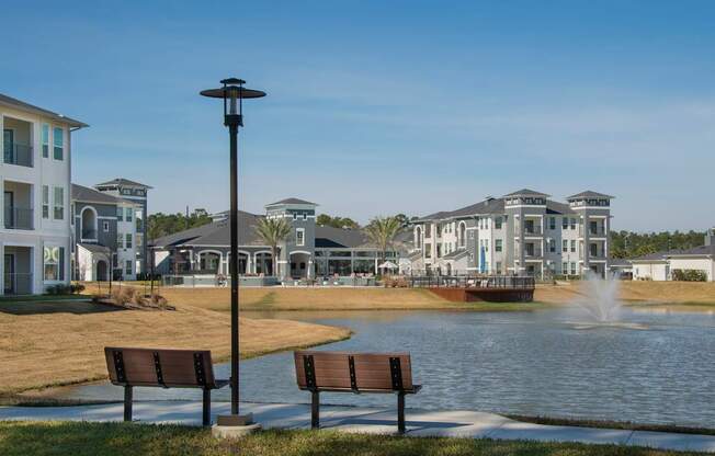 Two benches are in the foreground of a park with a pond and a fountain.