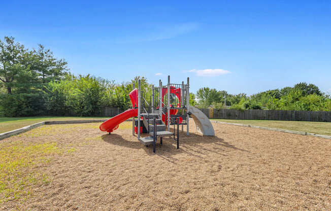 A playground with a red slide and a wooden structure.