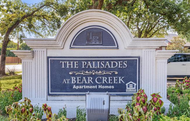 Sign for "The Palisades at Bear Creek Apartment Homes" featuring decorative elements and landscaping around the base.
