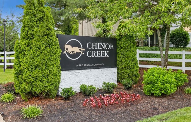 A sign for Chinook Creek in front of a white fence.