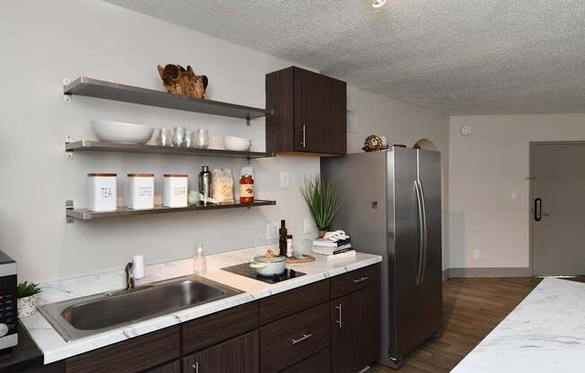 A kitchen with a sink, refrigerator, and shelves with various items.