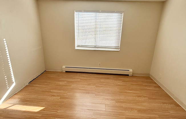 Bright and airy room featuring elegant wooden flooring, a ceiling fan, and a large window inviting natural light, perfect for a cozy living space.