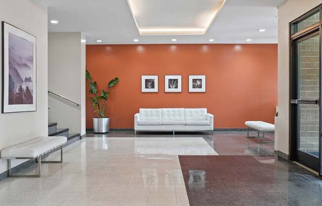 A white sofa sits in front of an orange wall in a modern hallway.