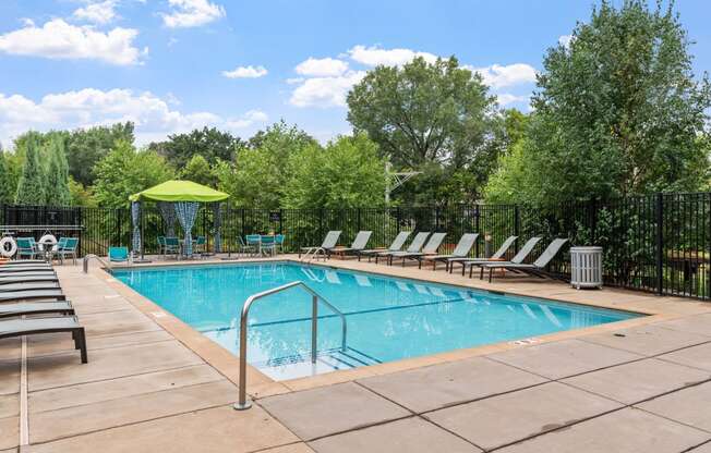 a swimming pool with chairs around it and trees in the background